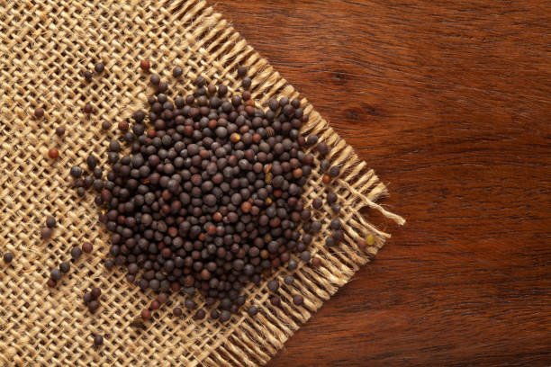 Macro close-up of Organic Black mustard seed (Brassica nigra)  on the wooden top background and jute mat. Pile of Indian Aromatic Spice. Top view